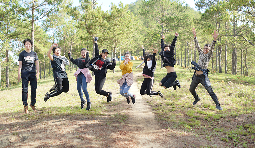 Eight teenagers are jumping in the forest path, green trees are in the background
